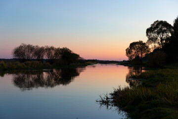Biebrza river at sunset, reflection in the water, silhouettes of trees reflecting in the calm water of the river. 
