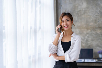 Beautiful and cute Asian business woman Office workers stand on the phone to talk and answer questions from customers in the office.