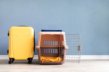 Opened plastic pet carrier or pet cage and yellow suitcase on the floor at home, copy space