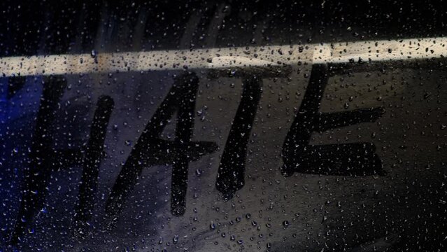 The word hate, written with a finger, on a misted night window