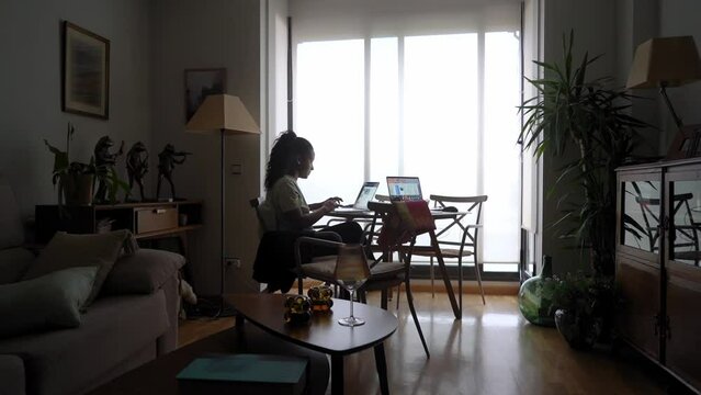 African american lady using laptop to work while being on holidays. Girl sitting next to panoramic window. Freelancer traveler. Workaholic female starting an small business from home. Wide angle.