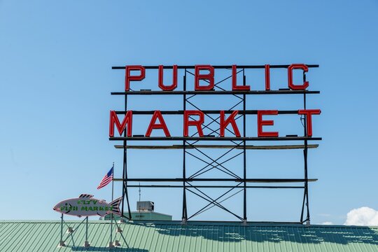 Red Public Market Sign With The American Flag Before The Blue Skyline In Seattle