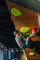A young, strong guy in a gray T-shirt and blue shorts of athletic build climbs a bouldering in a climbing center at a competition