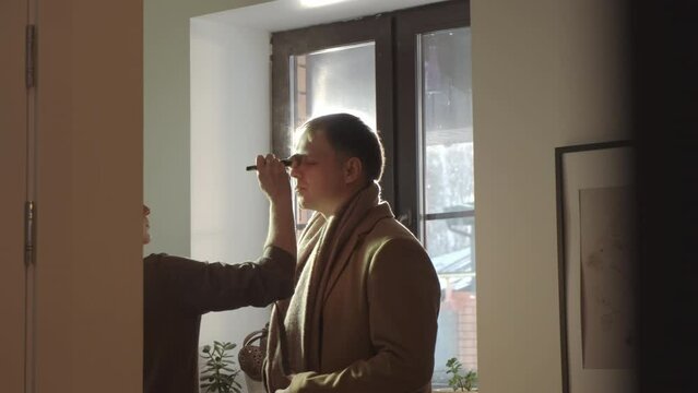 Medium of cropped makeup artist putting powder on face of male actor on movie set