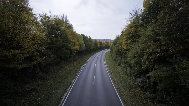 Traffic on a bend street between colorful trees in autumn with clouds time lapse
