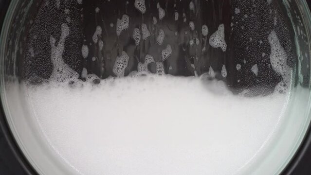 Close up clothes in washing machine with bubbles foam soap in laundromat shop