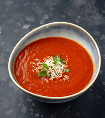 Nice ceramic bowl full of creamy and spicy tomato soup garnished with grated cheese and basil leaves