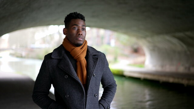 young black man walking under bridge wearing scarf and winter coat