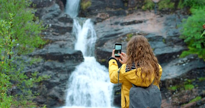 Nature, waterfall and woman with smartphone to take picture, travel and adventure with photography. Earth, forest and water with female back view and photograph, technology and hiking in mountains