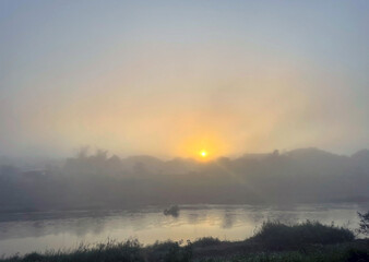 early morning river view the sun rises from the horizon in the east. Soft golden yellow sunlight hits the fog and steam. Soft and selective focus