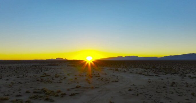 Sunset with the golden fiery orb of the sun just above the mountainous horizon in the Mojave Desert - push forward