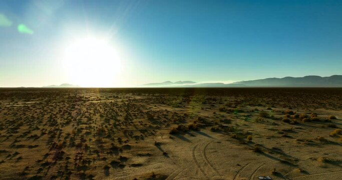 The sun shines brightly over the horizon of the vast Mojave Desert landscape - sliding aerial view