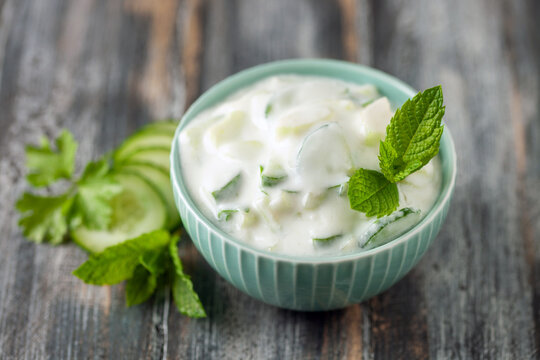 Indian Fresh sauce called Raita with herbs, dahi and sliced cucumber in a bowl on the table.