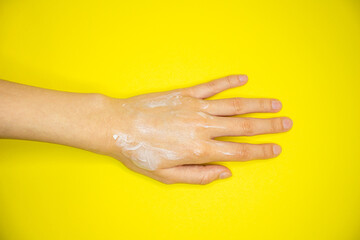 Fototapeta premium Moisturizing cream on woman's hand. Skin care concept. Isolated on yellow background. Top view.