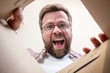 Happy man unpacks the delivered box with the parcel. Unpacking inside view.