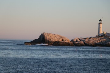 Sunset view of the Isles of Shoals Lighthouse on rocks surrounded by blue sea waves
