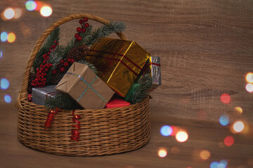 Wicker basket with gifts and spruce branches. Wooden background, beautiful colored bokeh in the upper left and lower right corners.
