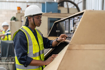 Young African American male engineer in vest and helmet safety checking and repairing old CNC machinery at factory Industrial.