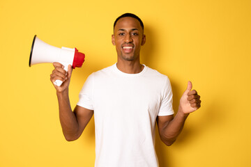 Young happy handsome african man holding megaphone with thumb up isolated over yellow background.