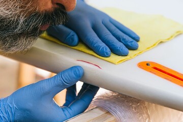 Closeup of a bearded surfer repairing a damaged part of a surfboard