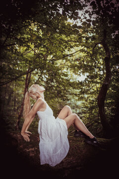 Blonde Frau weißes Kleid sitzt im Wald