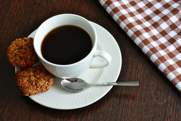 cup of coffee with white saucer, teaspoon and oatmeal cookies isolated, close-up