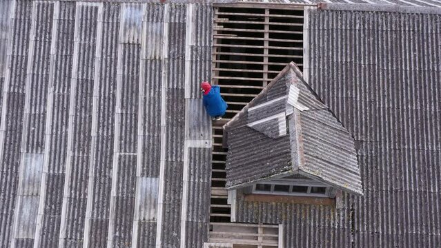 Worker repairing roof with sealant near mansard, aerial downwards view