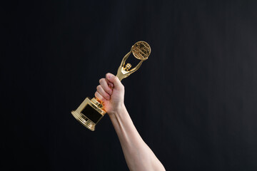 Hand holding golden statuette trophy on black background