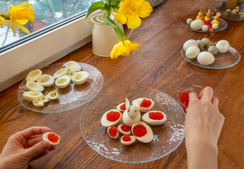 Step by step. egg rabbit figurine for decorationf, for making stuffed eggs. womens hands cut egg in half and fill eggs with red caviar. canapes with red caviar and quail eggs on a plate