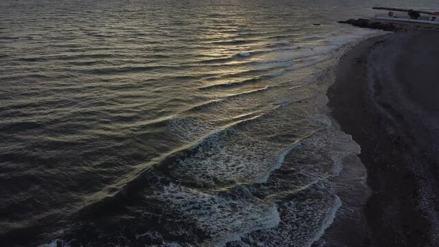 Drone footage of ocean waves crashing into the sandy beach in Torrox, Spain during sunset