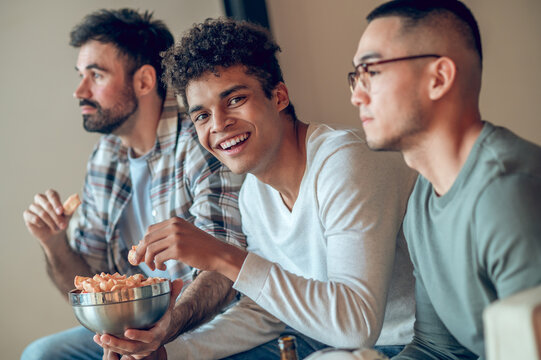 Merry guy snacking on chips in presence of his pals