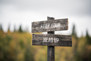 vintage and rustic wooden signpost with the weathered text quote keep your head up, outdoors in nature. blurred out forest fall colors in the background.