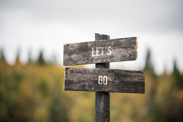 vintage and rustic wooden signpost with the weathered text quote lets go, outdoors in nature. blurred out forest fall colors in the background.