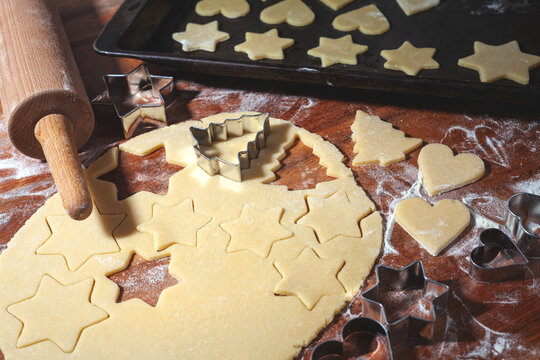 Weihnachtsb&auml;ckerei - aus hellem Teig werden auf einem Holztisch weihnachtliche Motive f&uuml;r Weihnachtspl&auml;tzchen ausgestochen