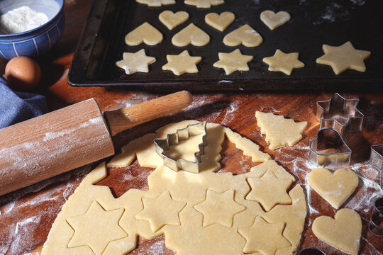 Weihnachtsb&auml;ckerei - aus hellem Teig werden auf einem Holztisch weihnachtliche Motive f&uuml;r Weihnachtspl&auml;tzchen ausgestochen