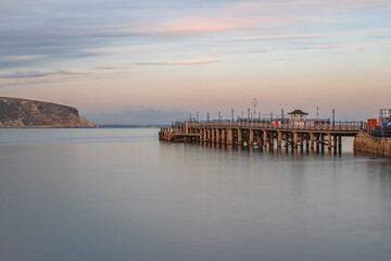 Obraz premium A clear November evening long exposure looking across smooth waters along Swanage Pier with a pink sky