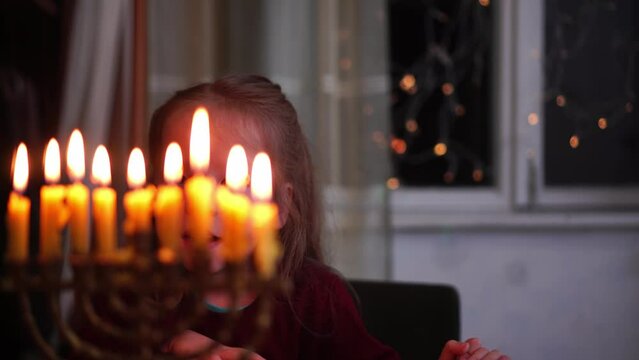 Hanukkah. Happy little jewish girl looks at the lights of the menorah