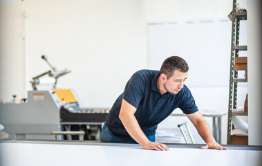 Professional worker printmaker technician operator works in printing press hall and printshop...