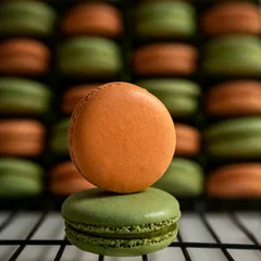 Zelfklevend Fotobehang Close-up view of orange and green sweet French macarons on the baking rack © Pjm Captures/Wirestock Creators