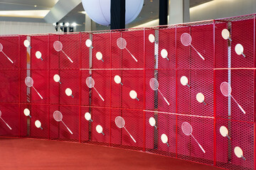 Table tennis and badminton rackets are hung on a red square grill steel grid, used as a backdrop...