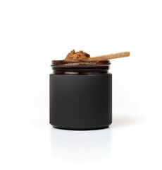 Jar with spice or supplement powder on spoon. Wooden spoon with brown powder on top of a small glass jar with plain black label. Healthy eating, vitamins and supplements concept. Selective focus.