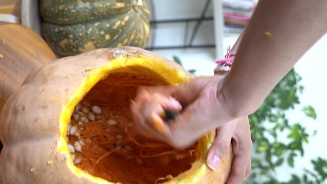 female carving large orange pumpkin for Halloween while sitting at wooden table at home