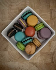 Zelfklevend Fotobehang Vertical top view of colorful macarons in the square bowl on a wooden surface © Pjm Captures/Wirestock Creators