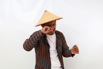 Disappointed asian farmer standing while holding little money and crying. Isolated on white background - obrazy, fototapety, plakaty