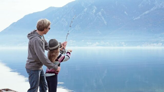 Father and daughter fishing. Family have fun together outdoors by lake, mountains. Parent supporting kid girl. Happy childhood, Fathers Day. Fishers with spinning rod by winter sea. Lifestyle moments