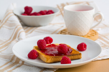 Toast with raspberry jam and cup of tea on beige table.