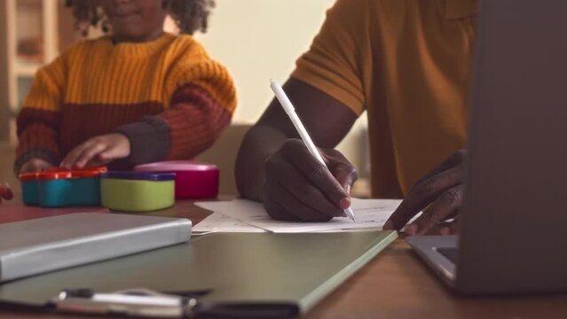 Cropped of cute African American girl playing with toys while her dad working with business documents at desk at home