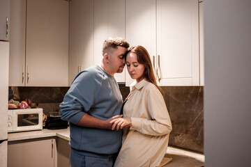 Romantic sexy young couple happily spending time hugging and kissing in cozy modern kitchen at home. Two people stand and joyfully look at each other