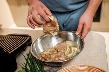 The man's hands prepares delicious juicy meat steak on an electric grill on wooden table. Smoke in the home kitchen