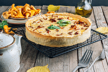 Homemade quiche or tart with chanterelles on rustic wooden background.
